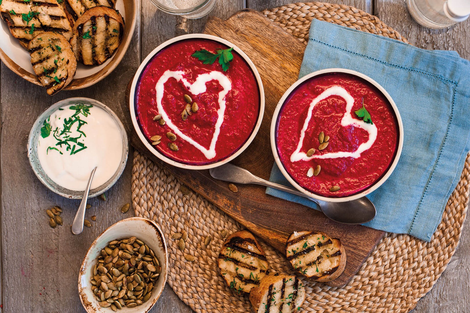 Two bowls of beetroot soup garnished with a heart of garlic yoghurt. Served with garlic bread